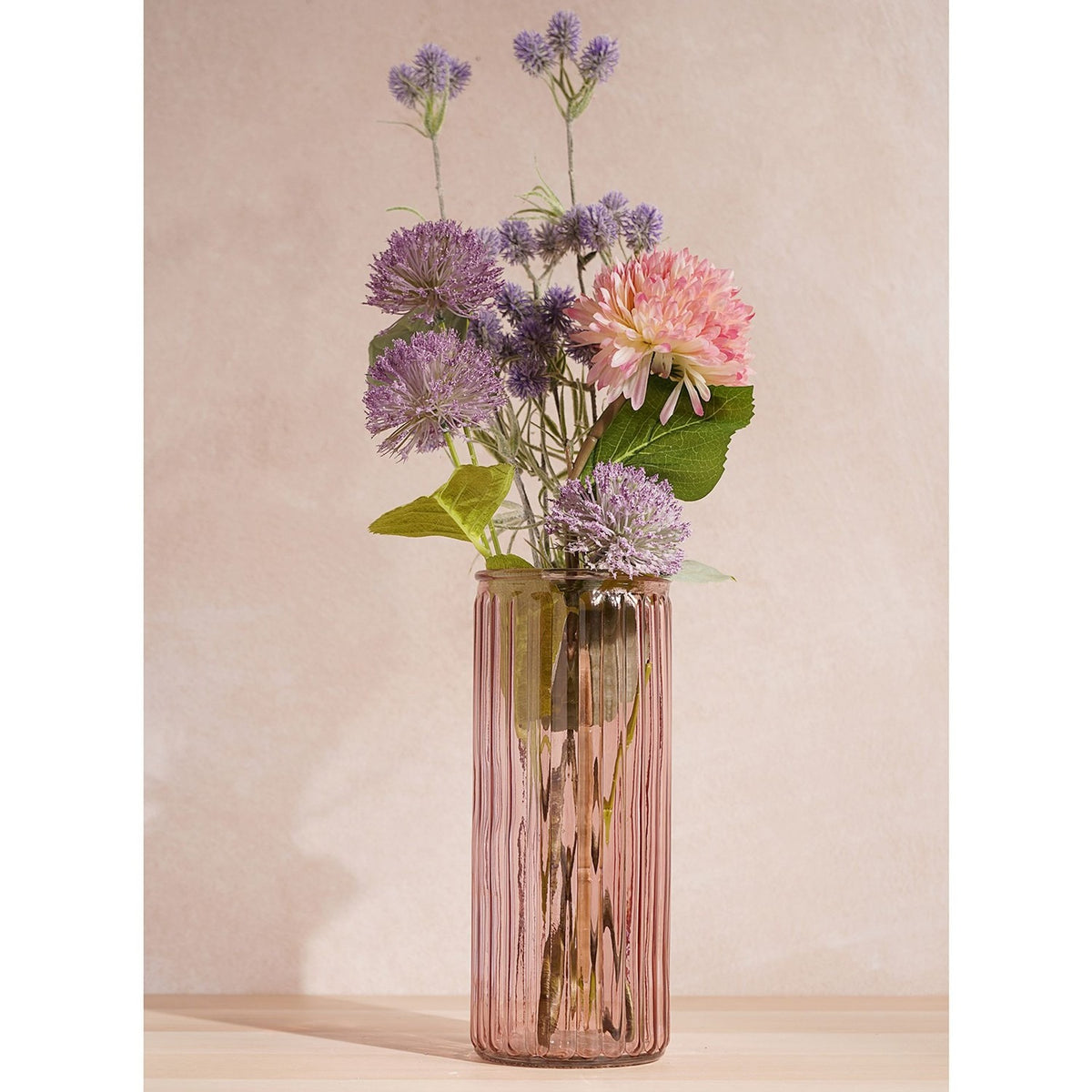 Tall ribbed cylindrical pink glass vase, 24.5cm, holding purple allium, pink dahlia and foliage stems against a plain neutral background.