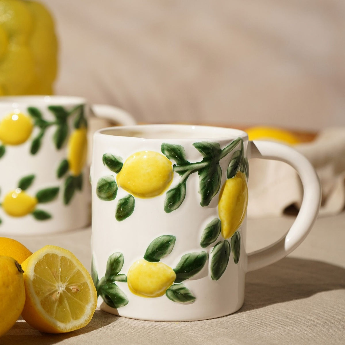 White ceramic mug with raised lemon and green leaf design, 600ml, shown beside fresh lemons on a neutral tabletop setting.