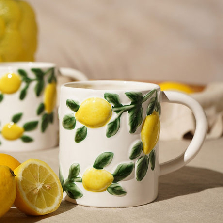 White ceramic mug with raised lemon and green leaf design, 600ml, shown beside fresh lemons on a neutral tabletop setting.