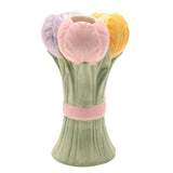 Ceramic vase shaped as a tulip bunch with lilac, pink, and yellow blooms on sage green stems tied with a raised pink bow, shown on a white background.