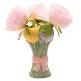 Ceramic vase shaped as three tulip blooms in yellow, lilac, and pink on sage green stems with a raised pink bow, shown with pink flowers on a white background.
