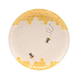 Round earthenware plate in cream with raised yellow honeycomb borders top and bottom, two striped bees and a dashed flight path across the centre, on a plain white background.