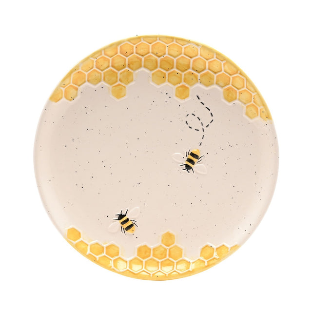Round earthenware plate in cream with raised yellow honeycomb borders top and bottom, two striped bees and a dashed flight path across the centre, on a plain white background.