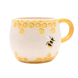 Cream earthenware mug with raised yellow honeycomb bands and a relief bee on the speckled body, finished with a yellow loop handle, shown on a white background.