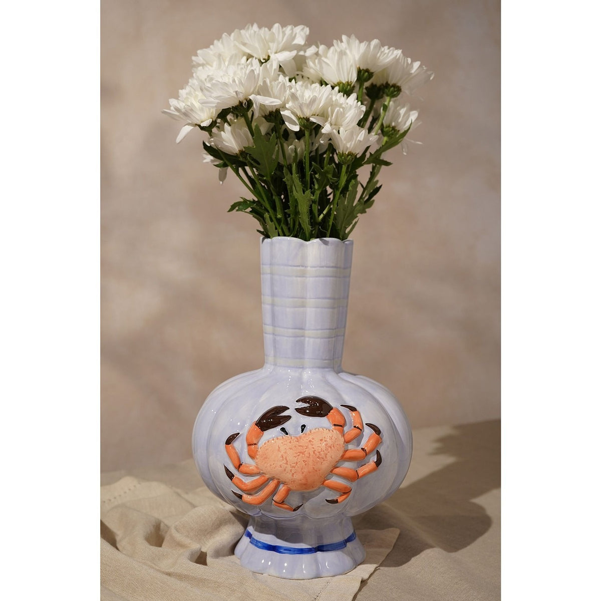 Hand-painted ceramic vase in periwinkle blue with a textured orange crab design, ribbed body, fluted scalloped neck, and blue-banded base, styled with white flowers.