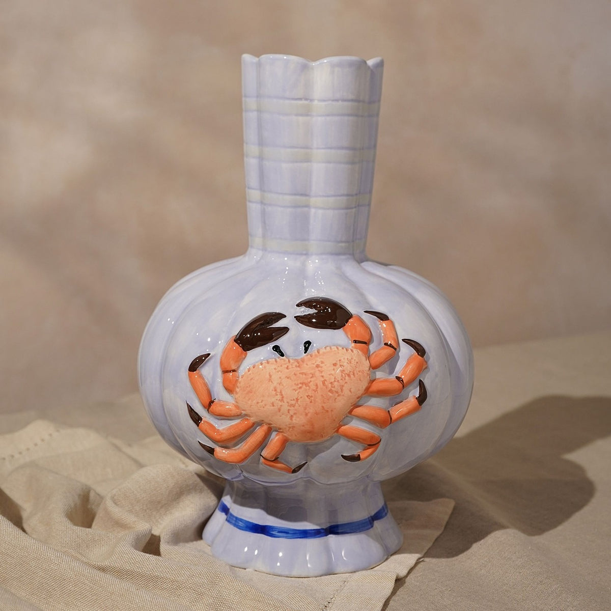 Hand-painted ceramic vase in periwinkle blue with a ribbed, lobed body, fluted scalloped rim, and a raised textured orange crab with dark-tipped claws across the front.