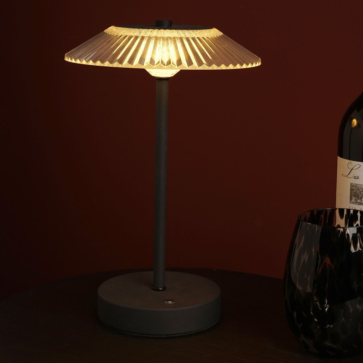 Ribbed Glass USB LED Touch Table Lamp with a wide fluted clear shade, slim black stem and round black base, shown lit on a dark table beside a wine bottle and glass.