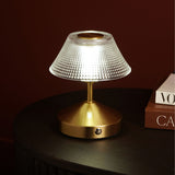 Small table lamp with a diamond-etched glass shade and brushed bronze base with touch control, shown lit on a dark table beside stacked books.