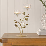 Floral Branch Double Metal Candle Holder in gold with clear ribbed glass cups, styled on a wooden sideboard with books and a decorative flower ornament.