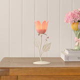 Floral Single Candle Holder with Metal Leaves in pink and cream, featuring a tulip-shaped cup on a slender stem with leaf details, shown lit on a wooden sideboard beside books and a flower vase.