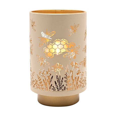 Cylindrical LED table lamp, 15.3cm, cream shade with cut-out bee, honeycomb and wildflower design illuminated from within, on a gold base, shown on a plain white background.