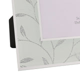 Close-up of a rectangular glass photo frame with glitter silver leaf and vine design on a frosted white border, white edge, and easel stand back.
