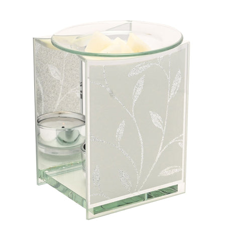 Glass wax melt burner with frosted white glitter leaf panels, mirrored sides, a tealight holder, and a clear glass dish holding wax melts on top, shown on a plain background.