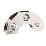 Arched mirrored silver glass candle holder with three round cut-outs holding lit tealights and scattered diamante detail at the lower corner, set against a plain white background.