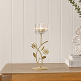 Floral Leaf Stem Metal Single Candle Holder in gold with a clear ribbed glass cup, shown lit on a round base with flower and leaf details on a wooden table.