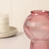 Ribbed Balloon Glass Vase with Flared Base in pink, close-up of the round ribbed body and neck, with a blurred ceramic jar and plate in the background.