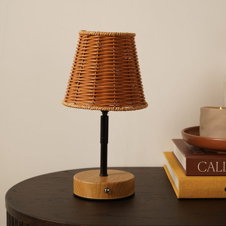 Wicker Shade LED Touch Table Lamp, 26.5cm, with tapered woven wooden-tone shade, slim black stem and round light wood base, shown on a dark table beside stacked books.