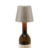 Round wine bottle topper LED table lamp in silver metal with a pleated tapered shade, shown fitted into a dark wine bottle neck on a white background.