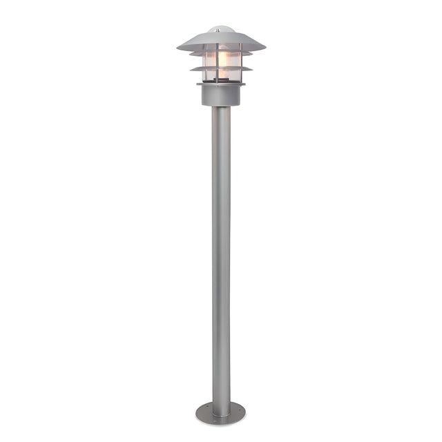 The Helsingor 1 Light Bollard Lantern in silver showcases Scandinavian design with its modern aesthetics, featuring a round, tiered lampshade and a visible light bulb. It's mounted on a sturdy cylindrical base, making it an ideal outdoor lighting fixture.