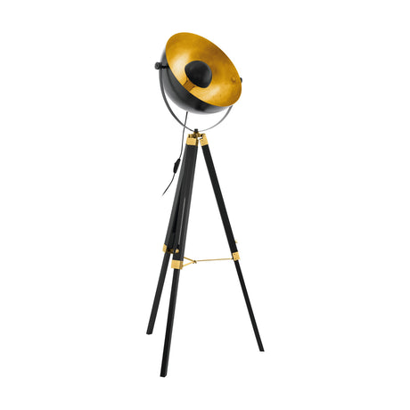Henorne tripod floor lamp with a black dome shade lined in gold, brass fittings and brace on black wooden legs, shown on a plain white background.