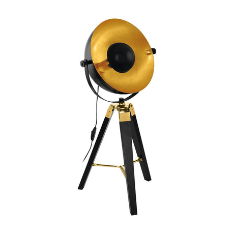 Henorne table lamp with a round black steel shade lined in gold, black wooden tripod legs and brass-toned joints, on a plain white background.