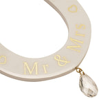 Close-up of cream MDF horseshoe wall art with gold "Mr & Mrs" lettering, outline hearts, and a faceted clear teardrop charm on a gold ring, shown against a white background.