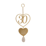Gold hanging plaque featuring an open heart framing the number 30, a smaller heart engraved 30 years of love and happiness, a faceted teardrop charm, and a top ring with chain.