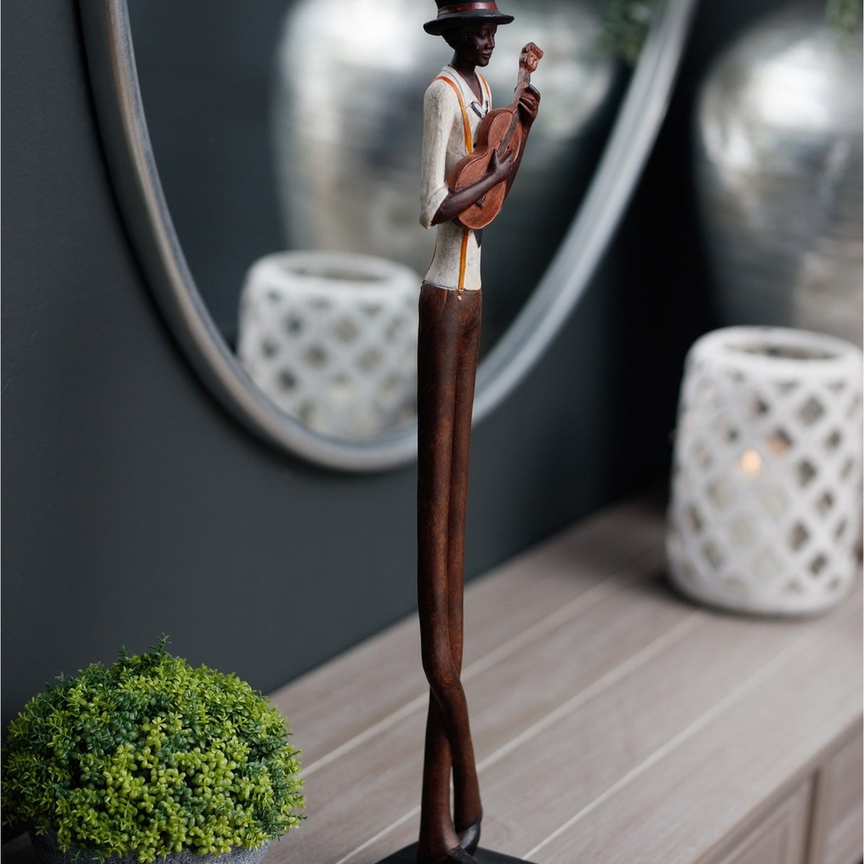 Hill Interiors Nerisse figurine of a tall, slim jazz musician in hat playing guitar, bronze and copper resin finish, styled on a console beside a mirror.