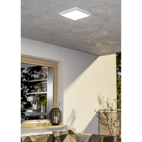 Hinanne LED Downlight, 28.5 x 28.5cm square white steel fixture with flush plastic diffuser, shown mounted on a textured grey ceiling above a bright living space.