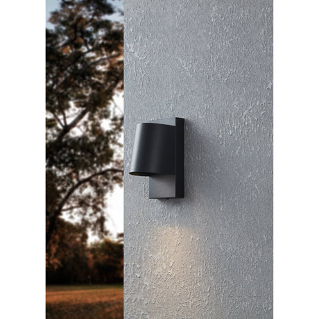 Hinvette outdoor wall light in black, aluminium and steel with a tapered round shade on a slim rectangular backplate, mounted on a textured grey exterior wall casting downward light.