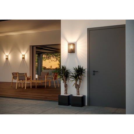 Hirbessa Outdoor Wall Light in black aluminium and steel with horizontal slats, shown illuminated beside a front door on a house exterior at dusk.