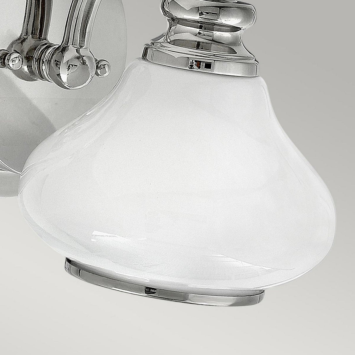 Close-up of the Ainsley 1 Light Wall Light, showcasing a polished chrome base and an opal glass shade, set against a neutral gray background.