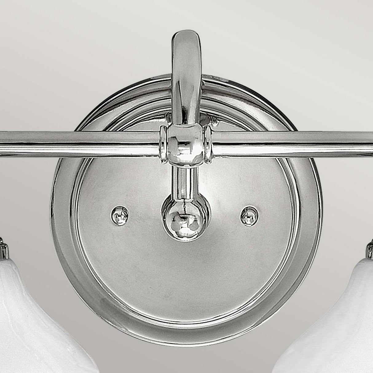 The Ainsley 2 Light Wall Light - Polished Chrome boasts a sleek, circular base from which two arms extend, each supporting an LED lamp adorned with a white fluted lampshade. Set against a neutral light gray background, the fixture exudes modern elegance.