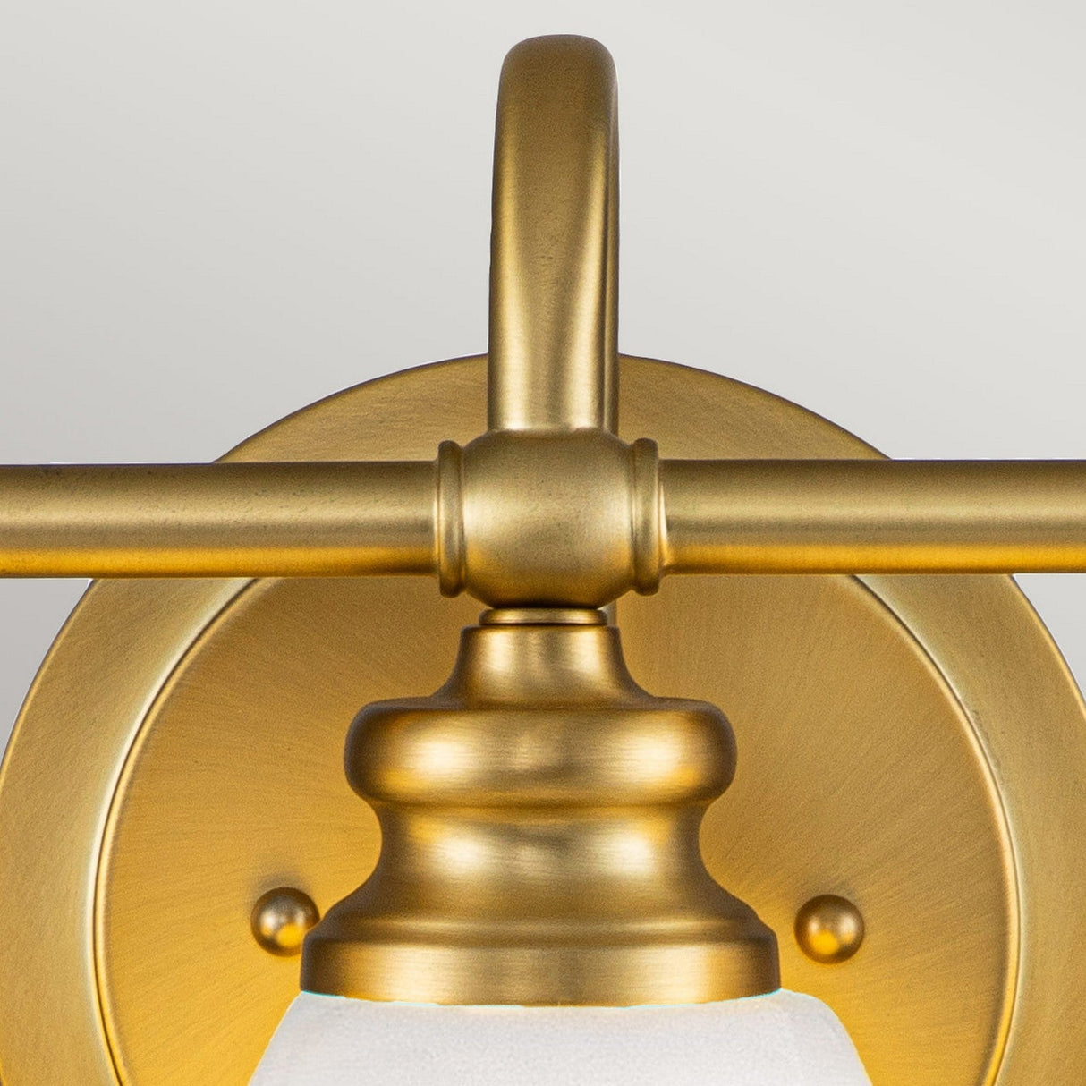 Introducing the Ainsley 3 Light Wall Light in Brushed Brass: This elegant fixture showcases a round wall mount paired with a curved arm, supporting an opal glass shade. With its brushed brass finish, it adds a timeless and sophisticated touch to any space. Equipped with energy-efficient LED lamps for enduring illumination, the fixture stands out against a light gray background.