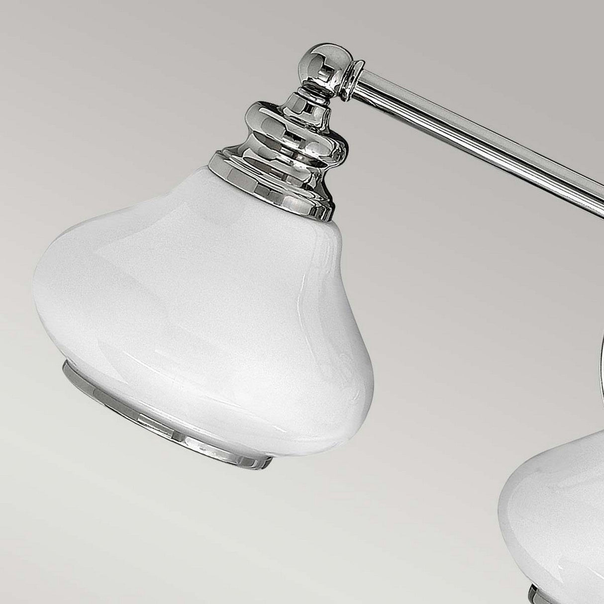 Close-up of the Ainsley 3 Light Wall Light in polished chrome, showcasing its glossy white, bell-shaped lampshades. The neutral gray background accentuates the sleek design and is elegantly complemented by energy-efficient LED lamps.