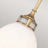 A close-up of the Amelia 1 Light Medium Pendant in Brass, showcasing its frosted glass shade that exudes vintage charm. The pendant features decorative cutouts near the top, blending modern farmhouse elegance against a plain background to accentuate its sophisticated yet timeless appeal.