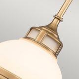 A close-up of the Amelia 1 Light Mini Pendant - Brass highlights its vintage style with an intricate cast glass fitter. The opal glass dome emits a soft, elegant glow, beautifully contrasted against a gray background.