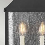 Close-up of the Beacon Hill 2 Light Outdoor Half Wall Lantern - Black, featuring two candle-like bulbs glowing behind a textured, speckled glass panel. The frame is crafted from Museum Black Aluminum, adding a sophisticated touch.