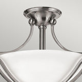 The Bolla 2 Light Semi Flush- Brushed Nickel fixture, ideal for sophisticated home decor, features a refined brushed nickel finish. Its smoothly curved white glass shade is elegantly upheld by three stylish metal arms extending from a central stem attached to a round ceiling mount.