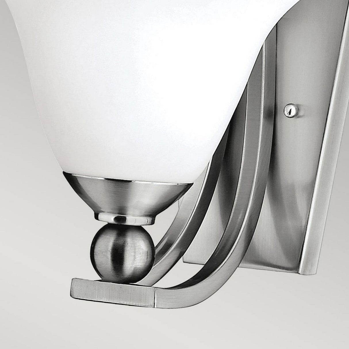 A close-up of the Bolla 1 Light Wall Light in brushed nickel showcases a modern design, featuring a white, curved glass shade and sleek metallic accents set on a rectangular base. This decorative piece exudes contemporary elegance.