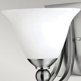 A close-up of the Bolla 1 Light Wall Light in brushed nickel highlights a decorative accent with a frosted, bell-shaped glass shade and a sleek metal base set against a light grey background.