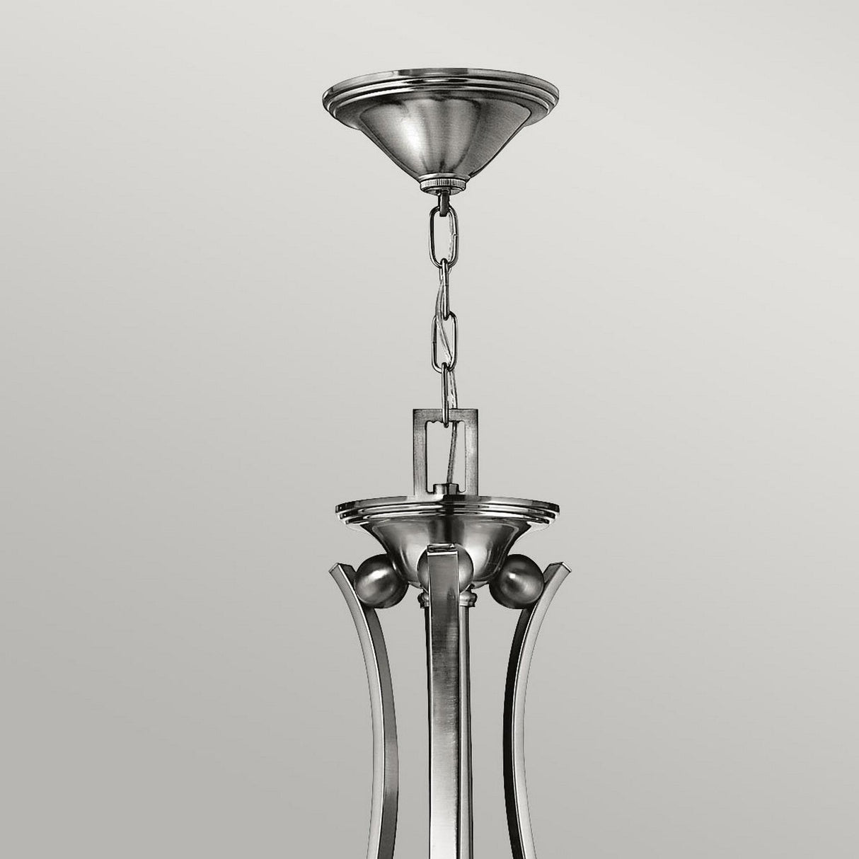 The Bolla 9 Light Chandelier - Brushed Nickel is showcased in close-up, highlighting its bell-shaped glass shades and metal chain. This modern fixture, known for its decorative details, stands out against a plain gray background with its sleek and minimalist design.