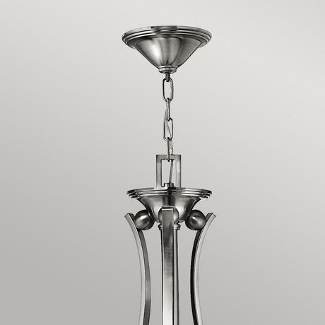The Bolla 9 Light Chandelier - Brushed Nickel is showcased in close-up, highlighting its bell-shaped glass shades and metal chain. This modern fixture, known for its decorative details, stands out against a plain gray background with its sleek and minimalist design.
