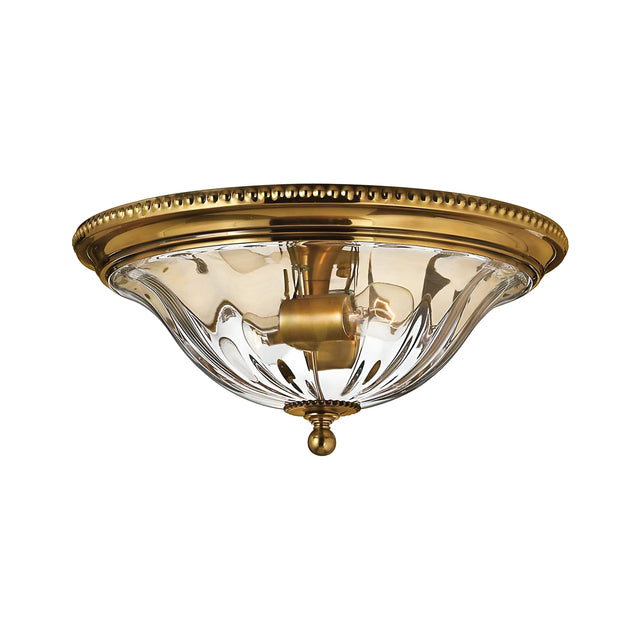 A detailed view of the Cambridge 2 Light Flush - Burnished Brass ceiling fixture, highlighting its decorative brass rim and clear, bowl-shaped glass shade that elegantly displays the light bulb. This piece is ideal for enhancing New England decor.