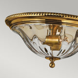 Close-up of the Cambridge 2 Light Flush - Burnished Brass chandelier, showcasing its textured glass dome and intricate gold detailing. The design highlights elegant gold beads around the edge and a central fixture for the lightbulbs, making it an ideal match for New England decor set against a pale gray background.