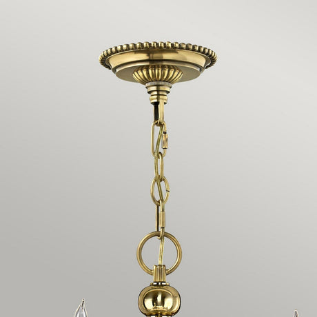 A close-up of a burnished brass ceiling mount showcases an elegant decorative design with a chain extending downwards. The round, polished links connect to a spherical ornament at the bottom. The plain, light gray background highlights the timeless allure reminiscent of the Cambridge 15 Light Chandelier - Burnished Brass.