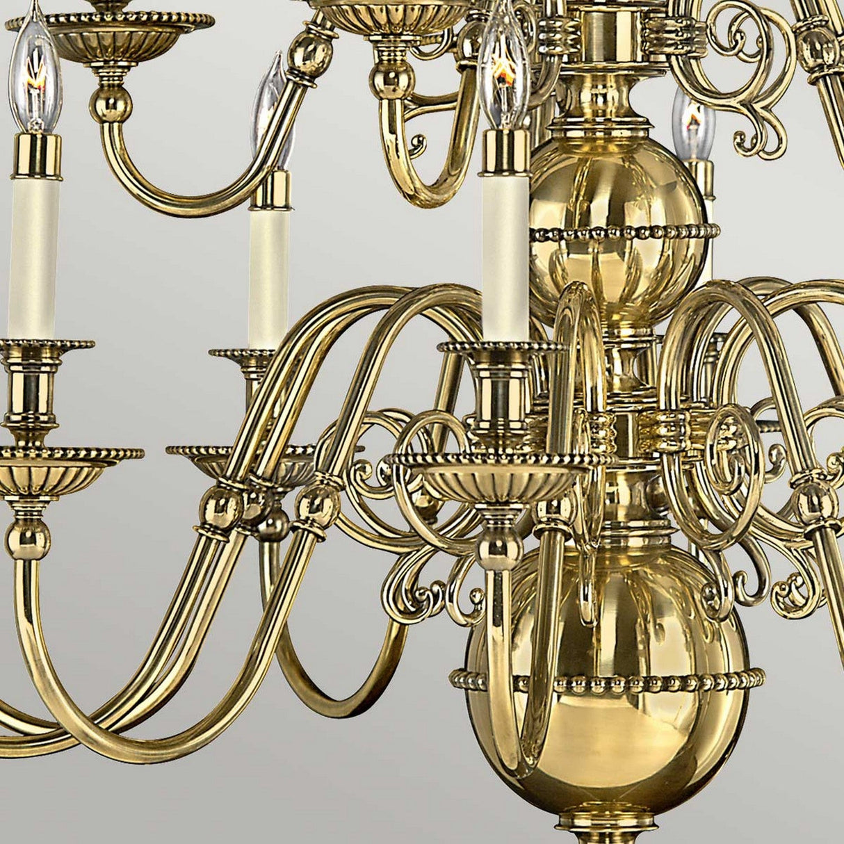 A detailed view of the Cambridge 15 Light Chandelier - Burnished Brass highlights its elaborate burnished brass finish with intricate scrollwork. Each gracefully curved arm holds multiple candle-style bulbs, set against a neutral background that accentuates its lustrous, reflective surface.