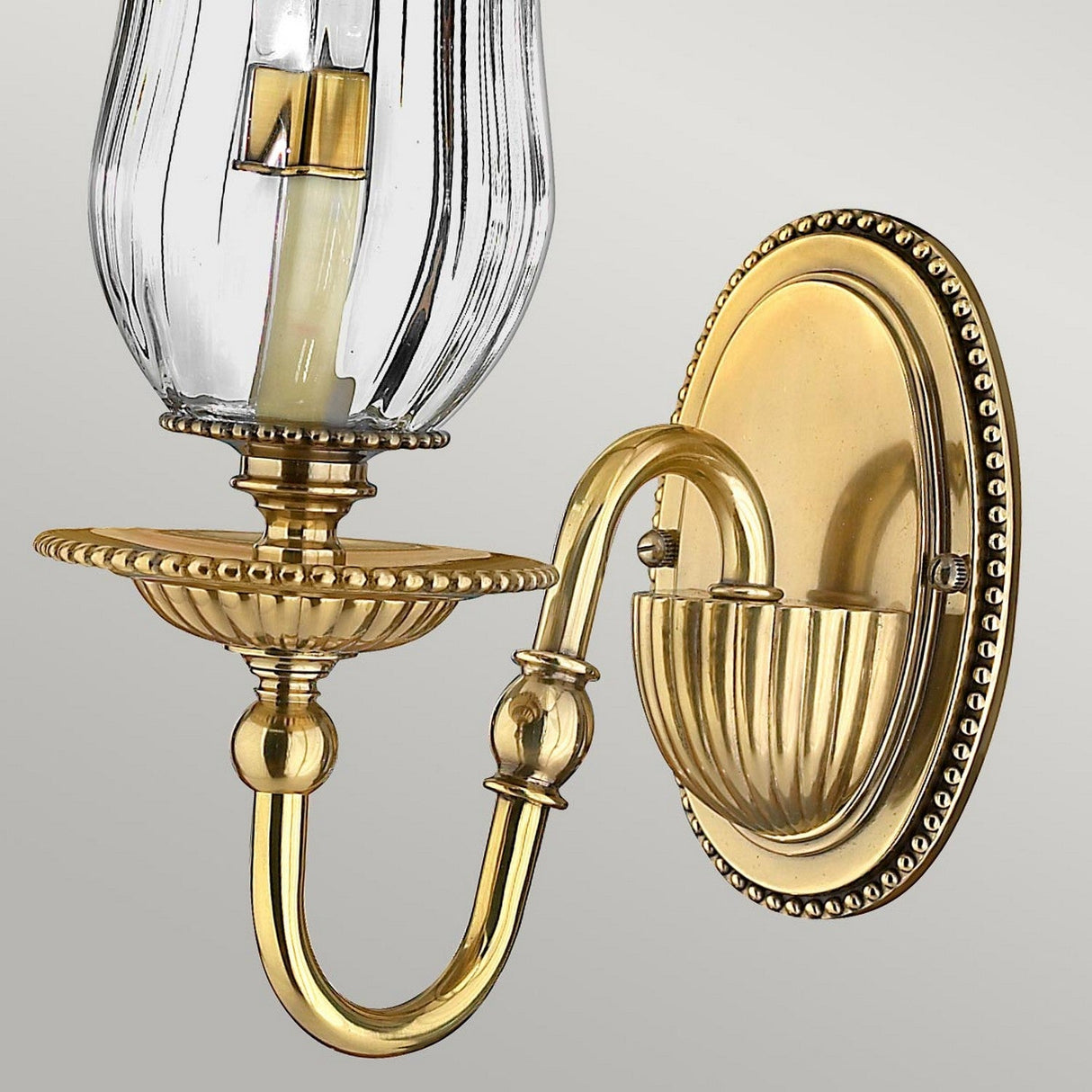 The Cambridge 1 Light Wall Light in Burnished Brass exudes classic New England charm with its elegant design. It includes a curved arm, decorative base, and clear glass shade, all crafted to accommodate a candle-shaped light bulb.