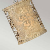 The Carabel 1 Light Mini Pendant in Brushed Champagne features intricate, ornate pierced metalwork and elegantly hangs at an angle against a gray background.