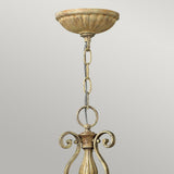 Elevate your space with the Carabel 3 Light Chandelier - Brushed Champagne, where elegant lighting is highlighted by an intricate metal fixture in a weathered gold hue that evokes brushed champagne. Its chain link configuration connects effortlessly to a round ceiling mount, all set against a gray backdrop.